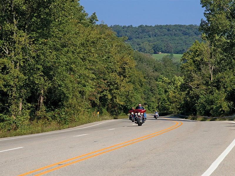 Motorcycle on a winding road surrounded by trees and hills.