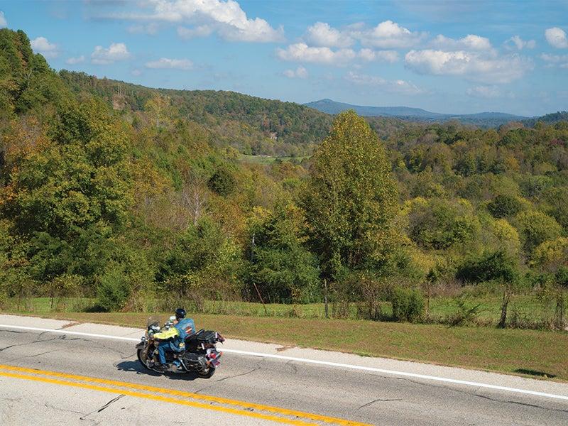 Motorcycle on a scenic road with rolling hills and green trees.