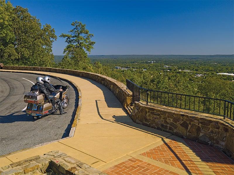 Motorcycle on a scenic overlook road with a vast green landscape.