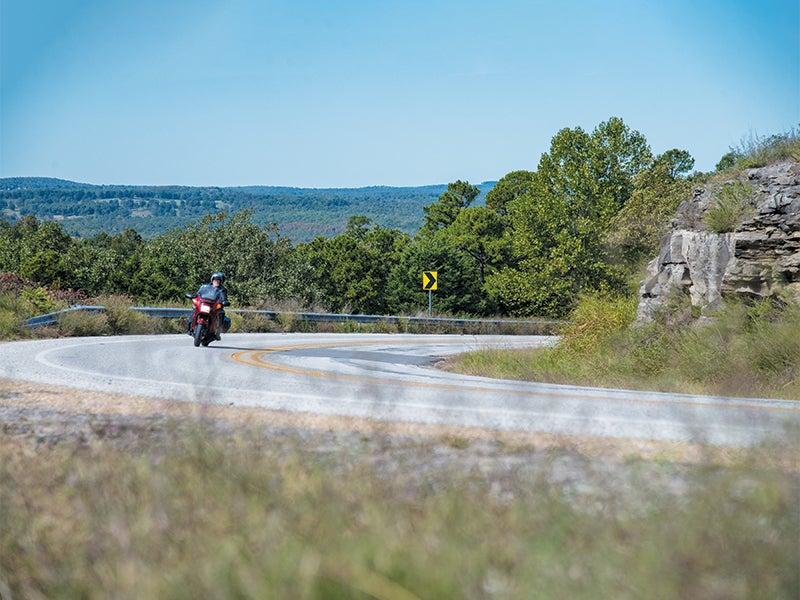 Motorcyclist on a scenic winding road with trees and blue sky.