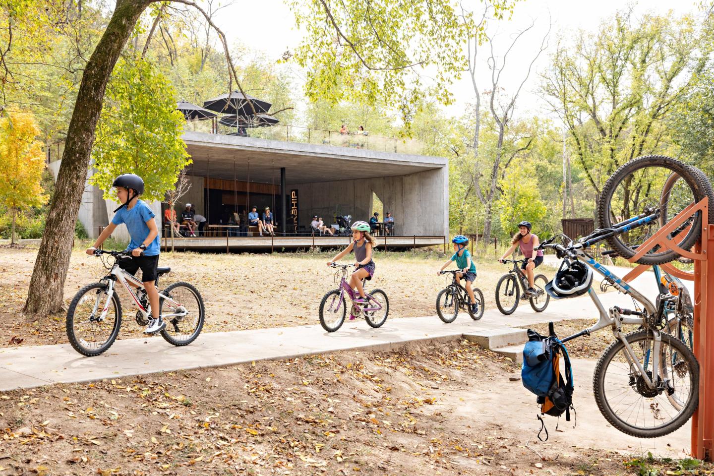 People cycling on a path near a modern building in a park.