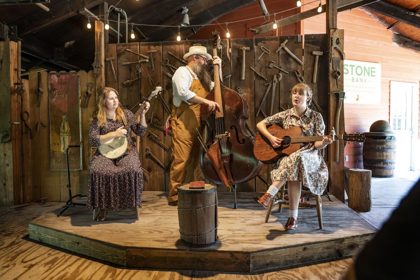 Rustic stage with three musicians playing banjo, double bass, and guitar.