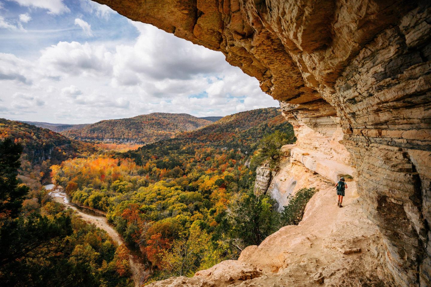 Climber on a cliffside with a vast, colorful autumn valley below.