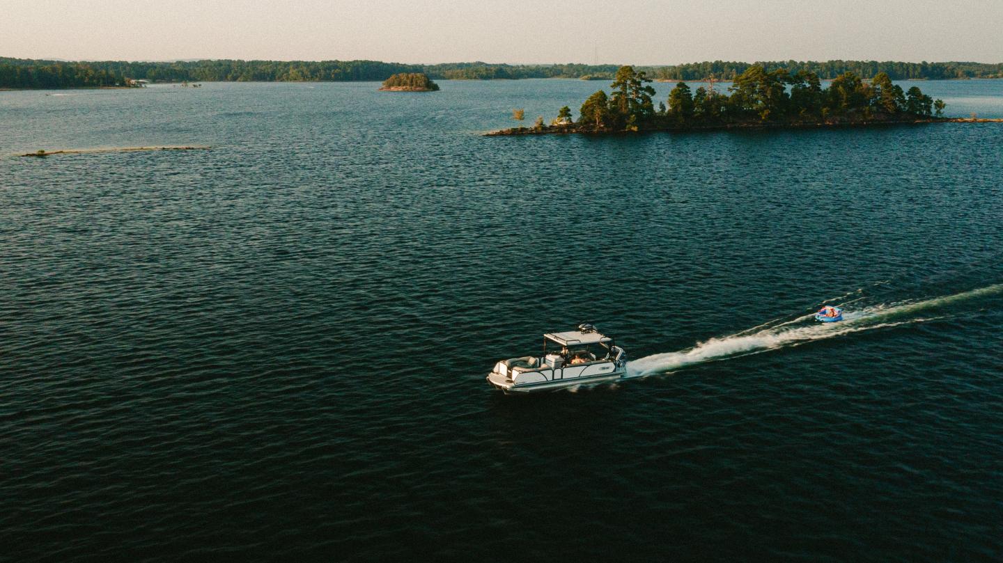 Boat cruising on a lake near small islands, under a clear sky.