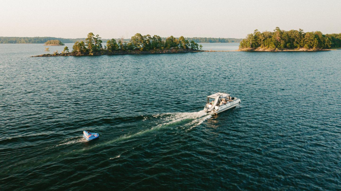 Boat pulling a jet ski on a lake with islands in the background.