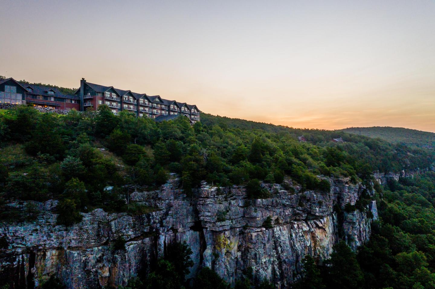 Clifftop lodge overlooking a forested canyon at sunset.