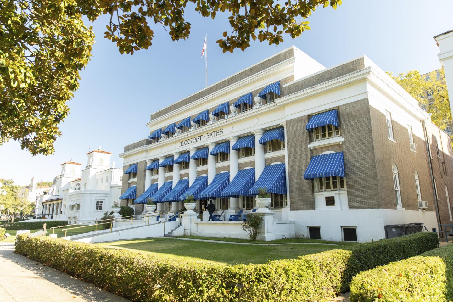 Grand building with blue awnings, sunny day, surrounded by greenery.