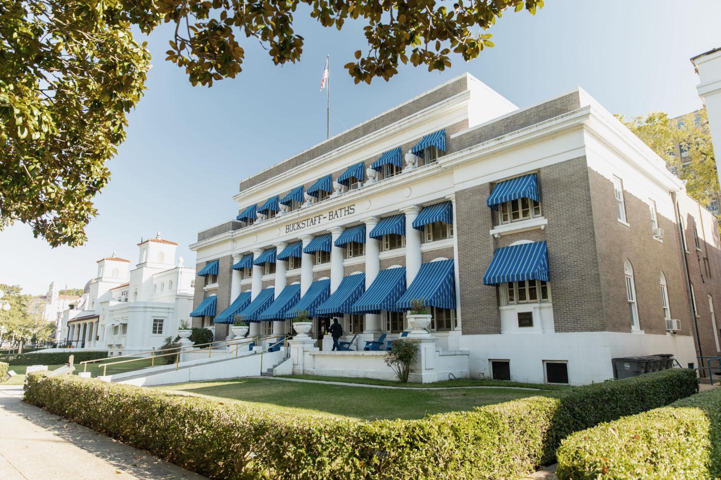 Historic building with blue awnings, surrounded by trees and hedges.