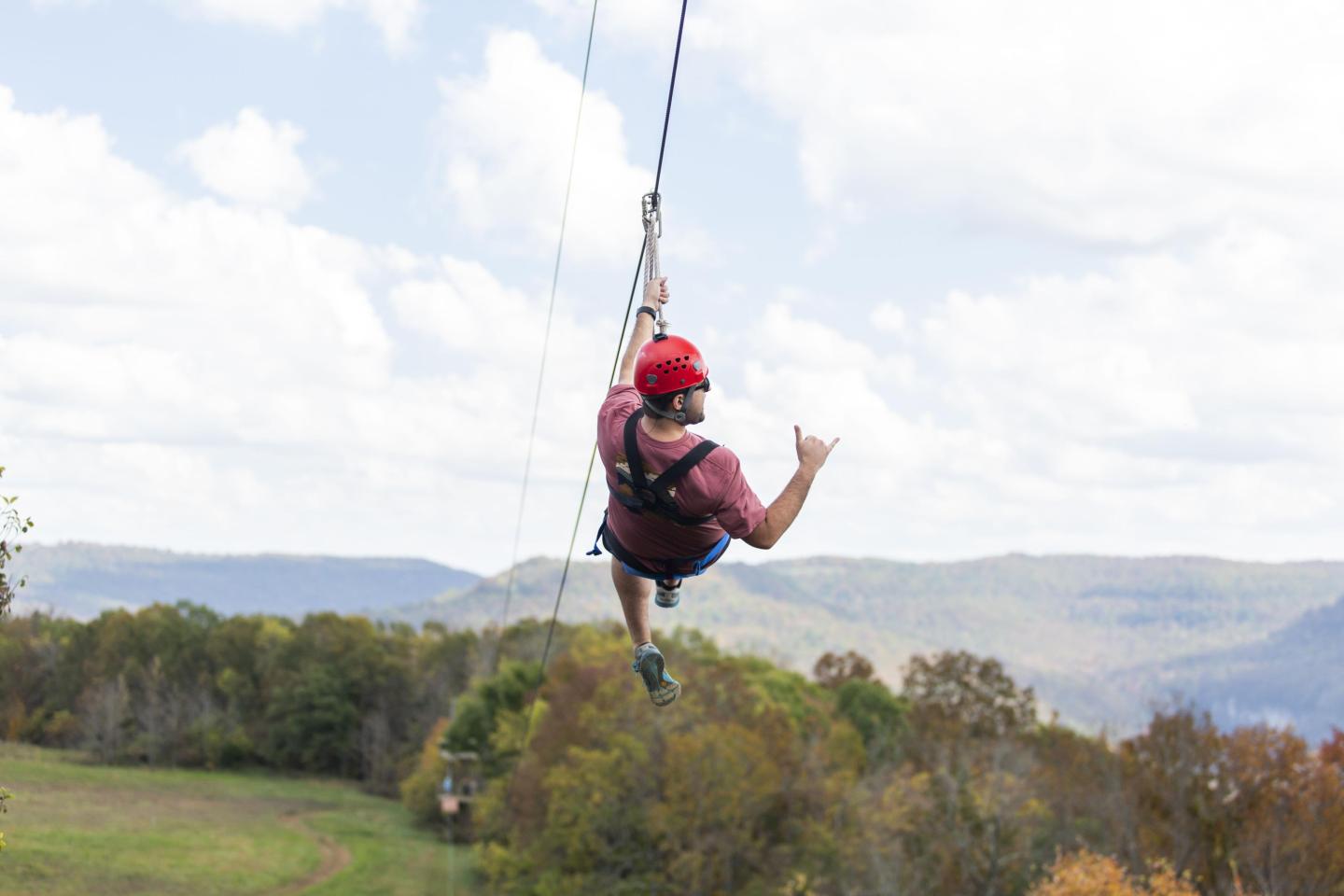 Person zip-lining over a scenic landscape with mountains and trees.
