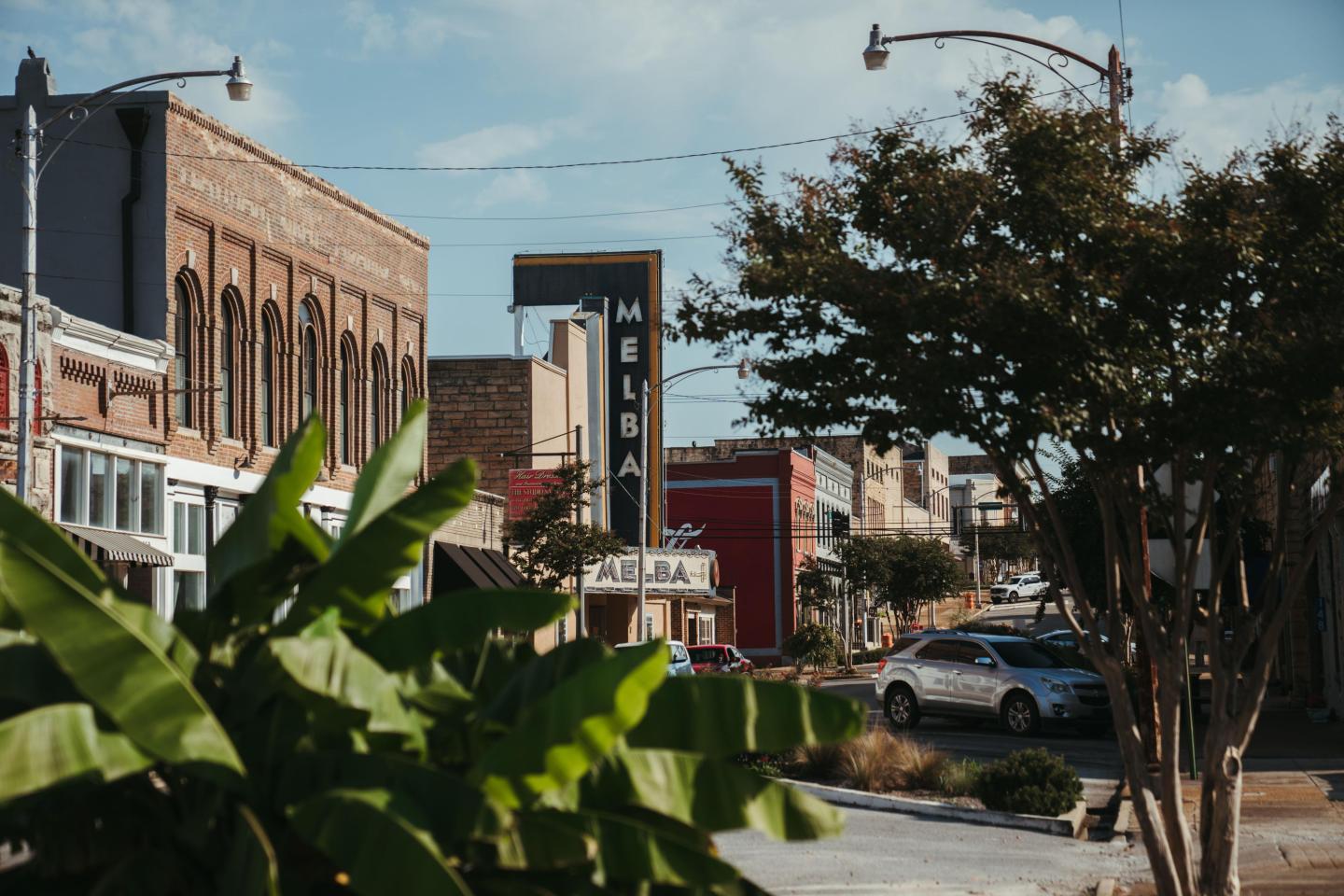 Small town street with trees and historic buildings, clear sky.
