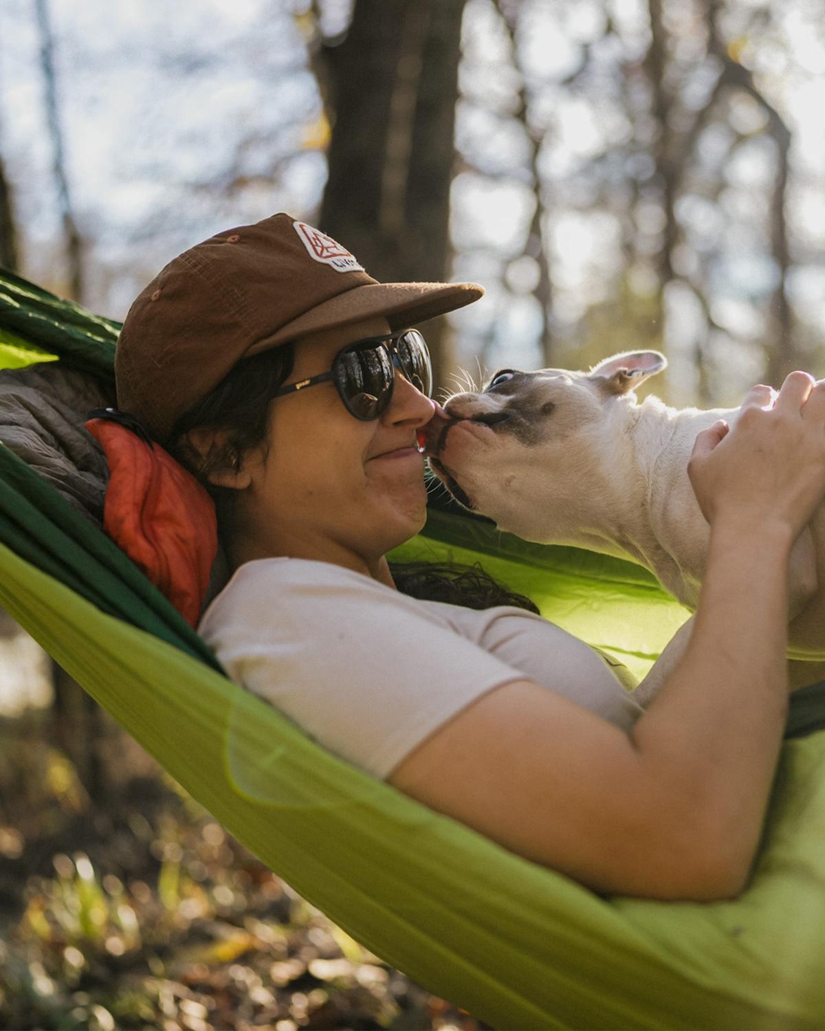 Woman in a hammock with a dog licking her face.
