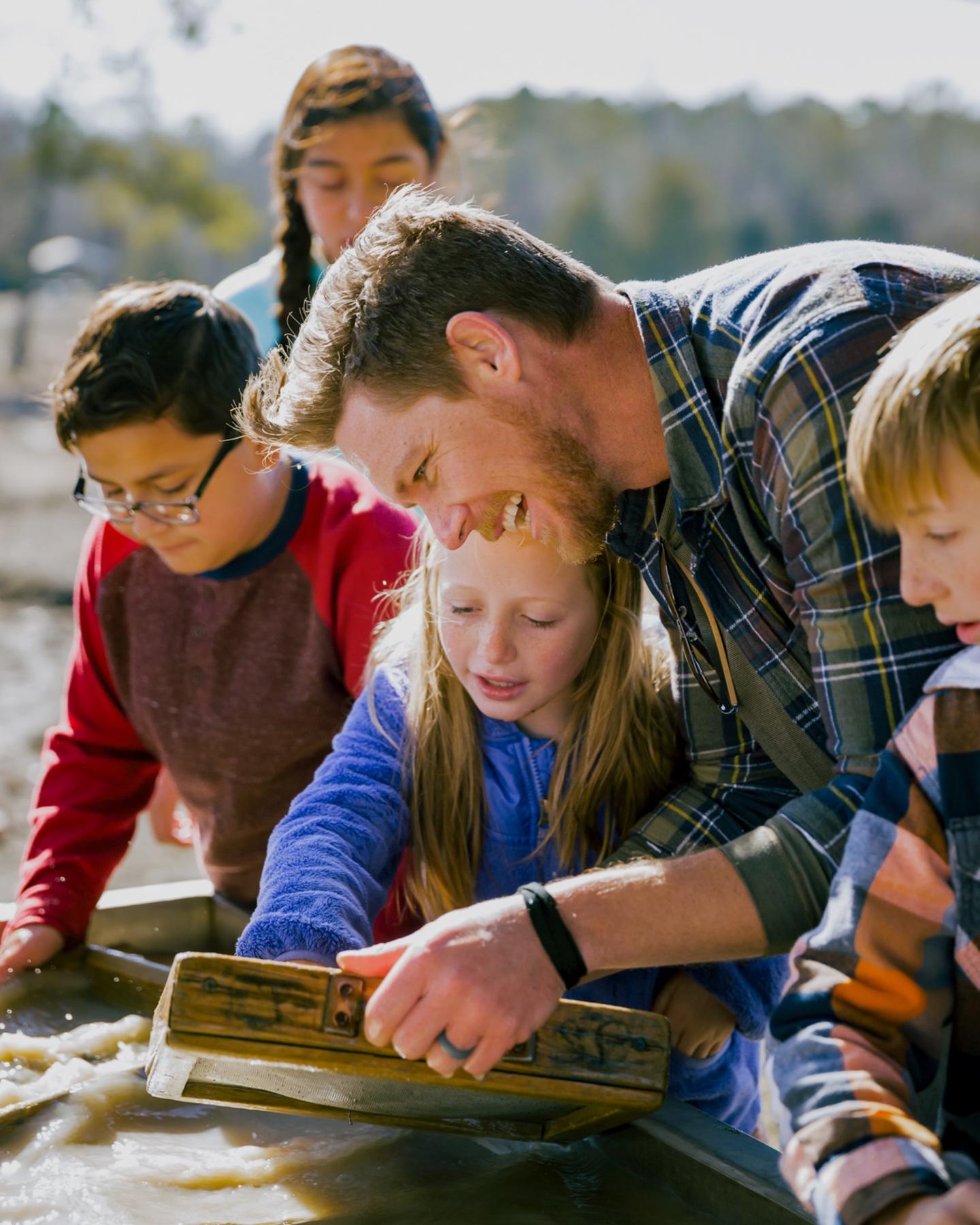 Adults and children panning for diamonds together outdoors.