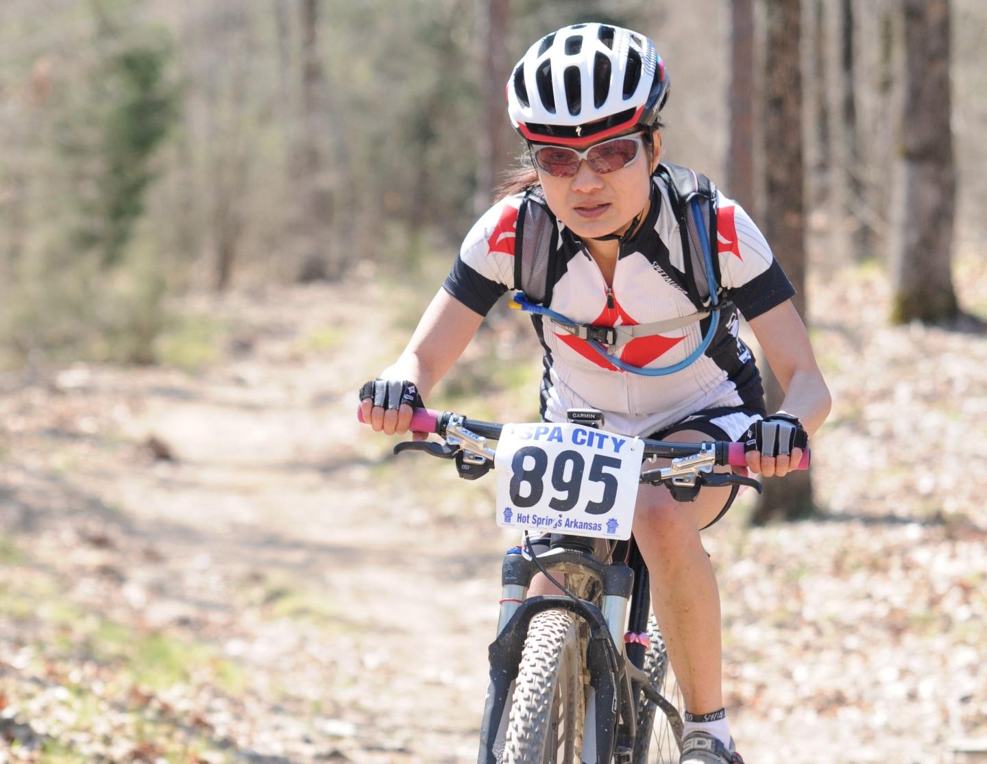 Cyclist in race on forest trail, wearing a helmet and sunglasses.
