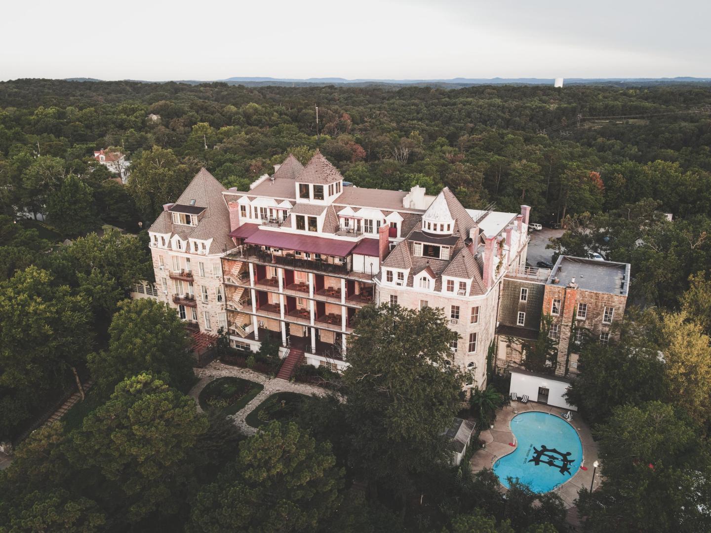 Historic building surrounded by trees, with a visible pool, under a cloudy sky.