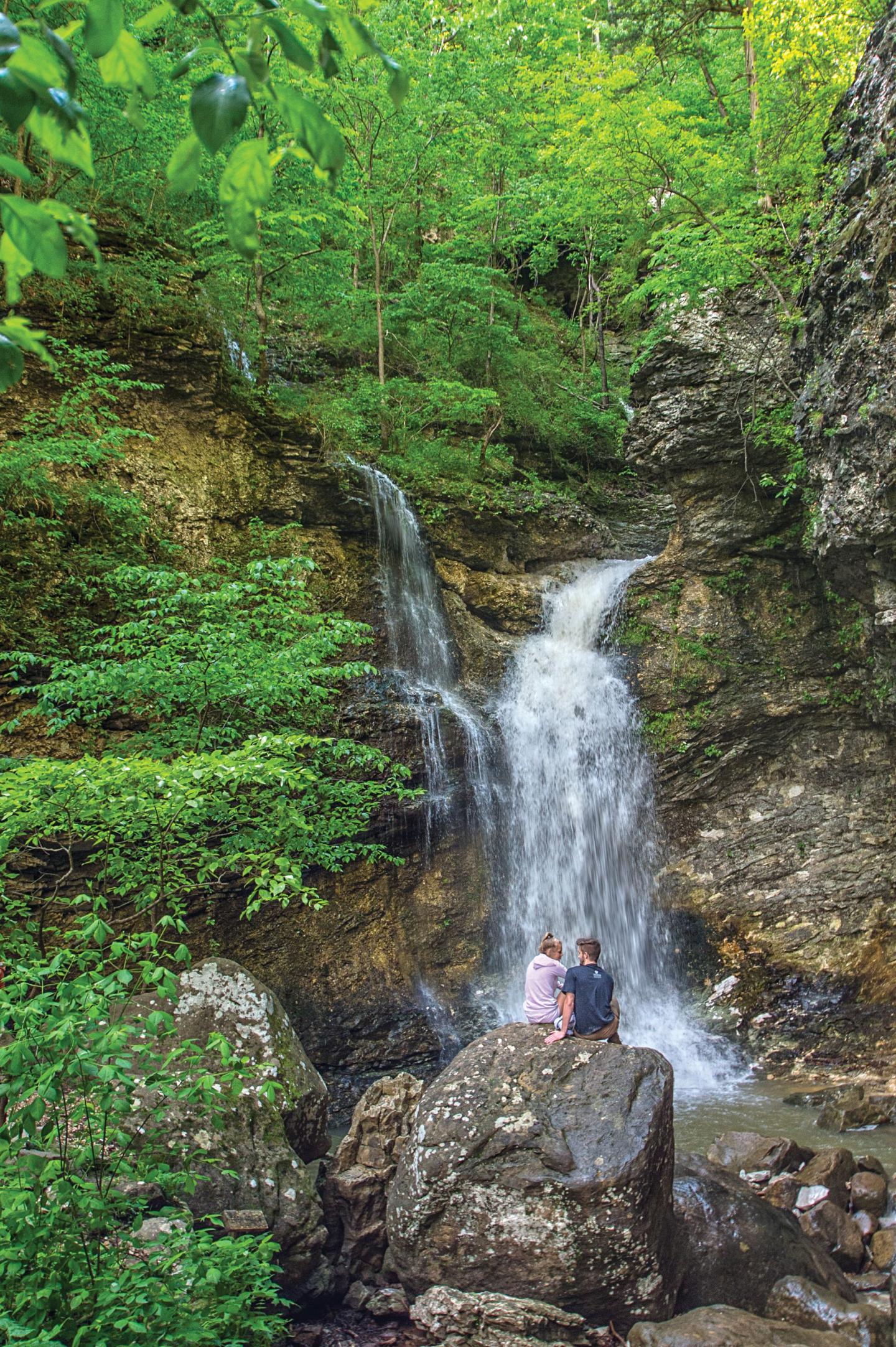 Couple sitting on rock by a forest waterfall.