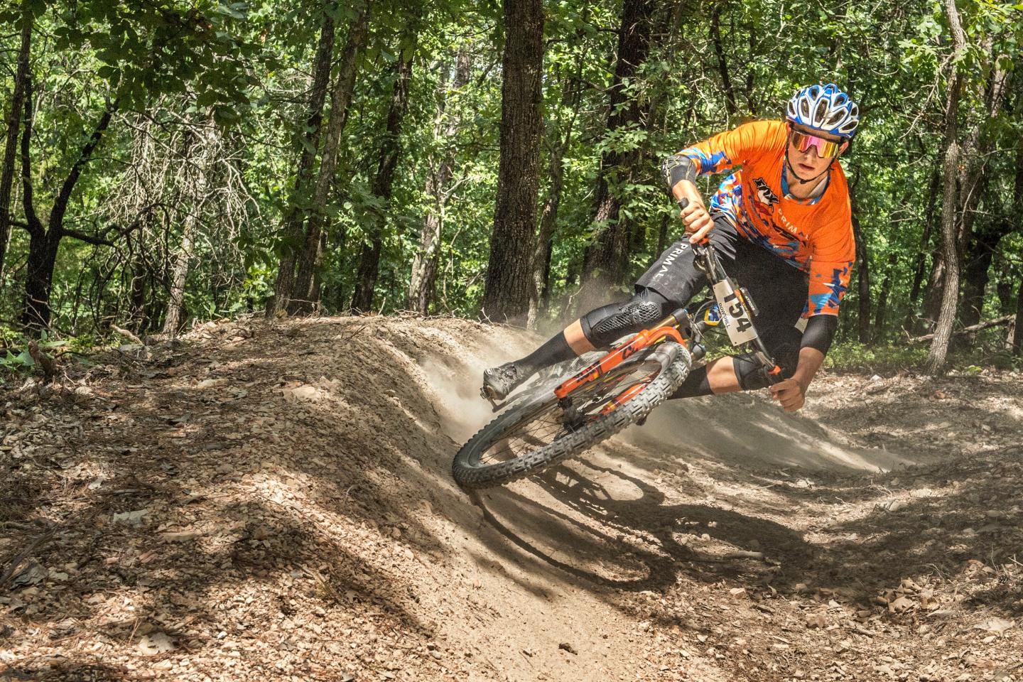 Mountain biker in orange jersey riding through forest trail.