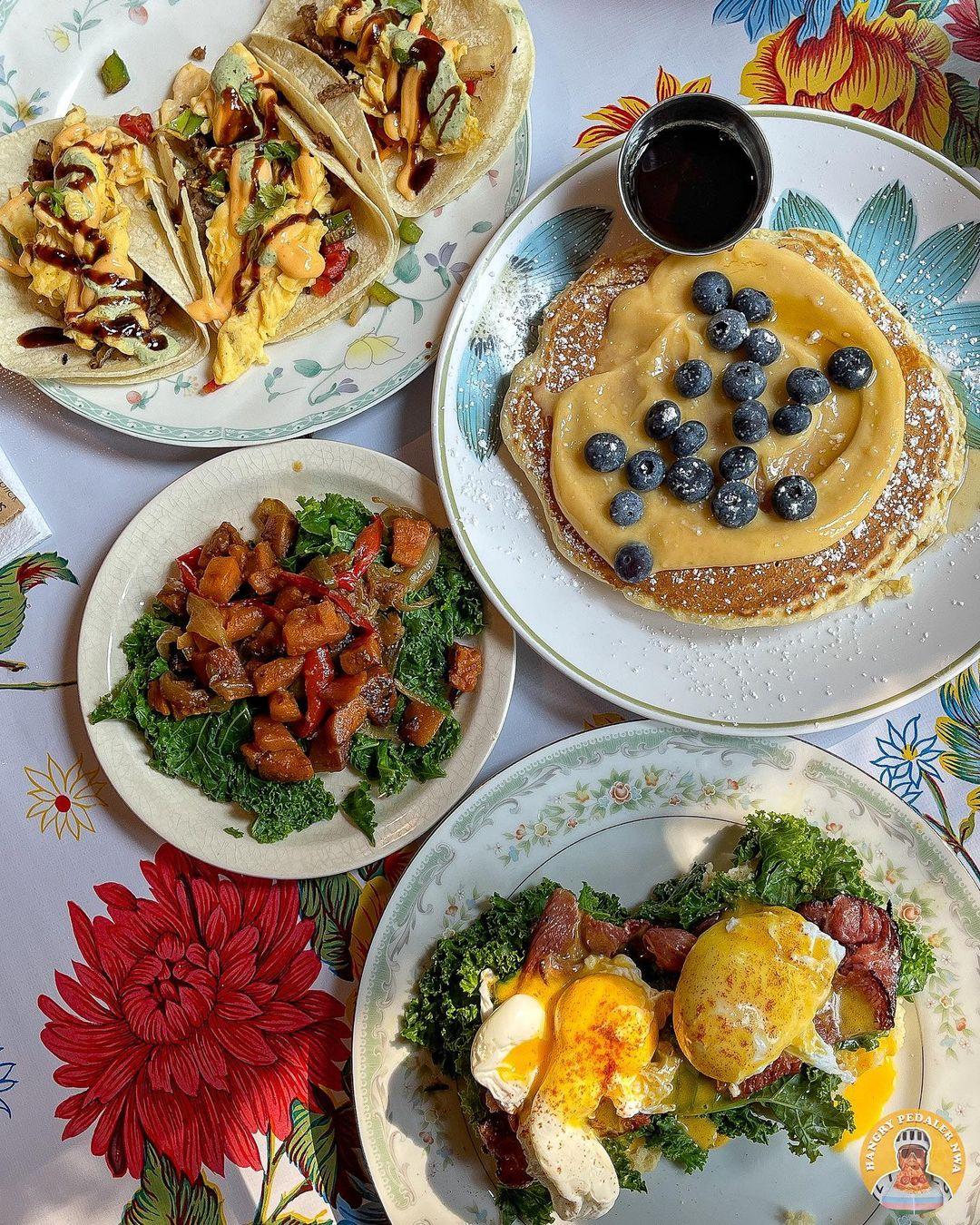 Tacos, blueberry pancakes, roasted potatoes, and eggs benedict on a floral tablecloth.