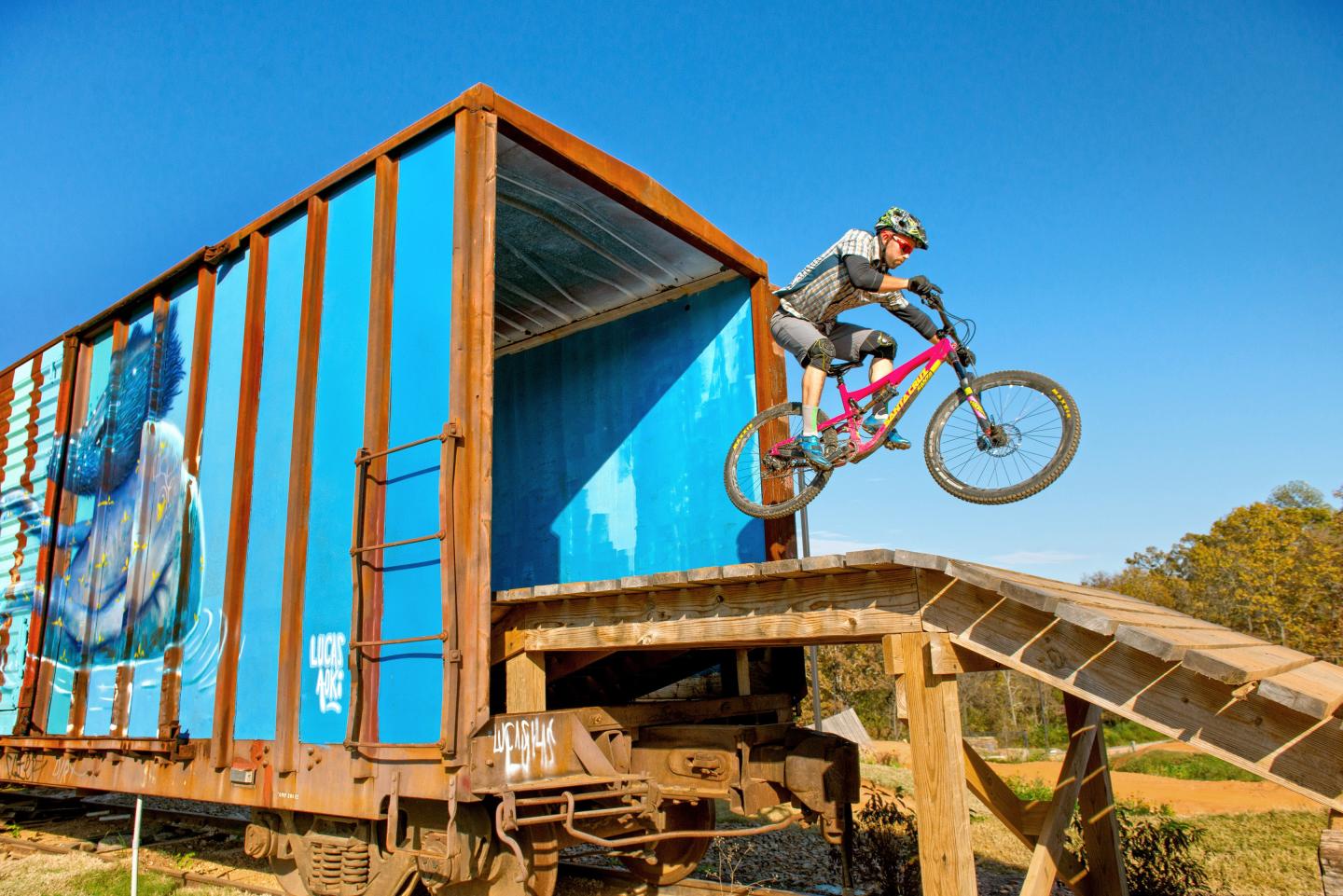 Cyclist riding off a ramp from a freight train, clear blue sky.