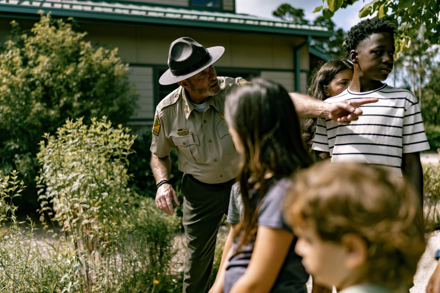 Park ranger guiding children outside in a garden.