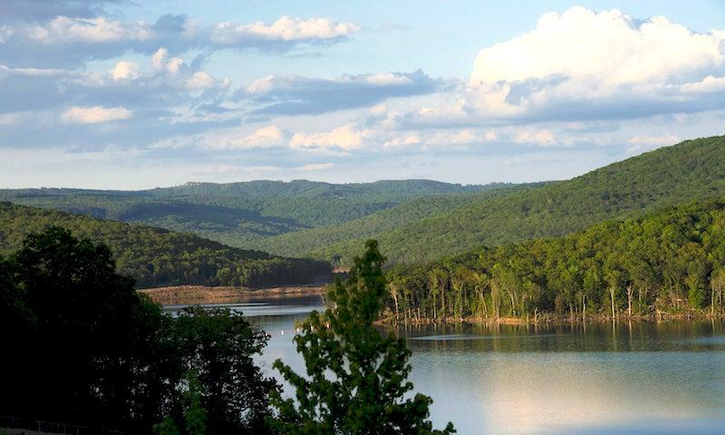 A serene lake surrounded by lush green hills under a partly cloudy sky.
