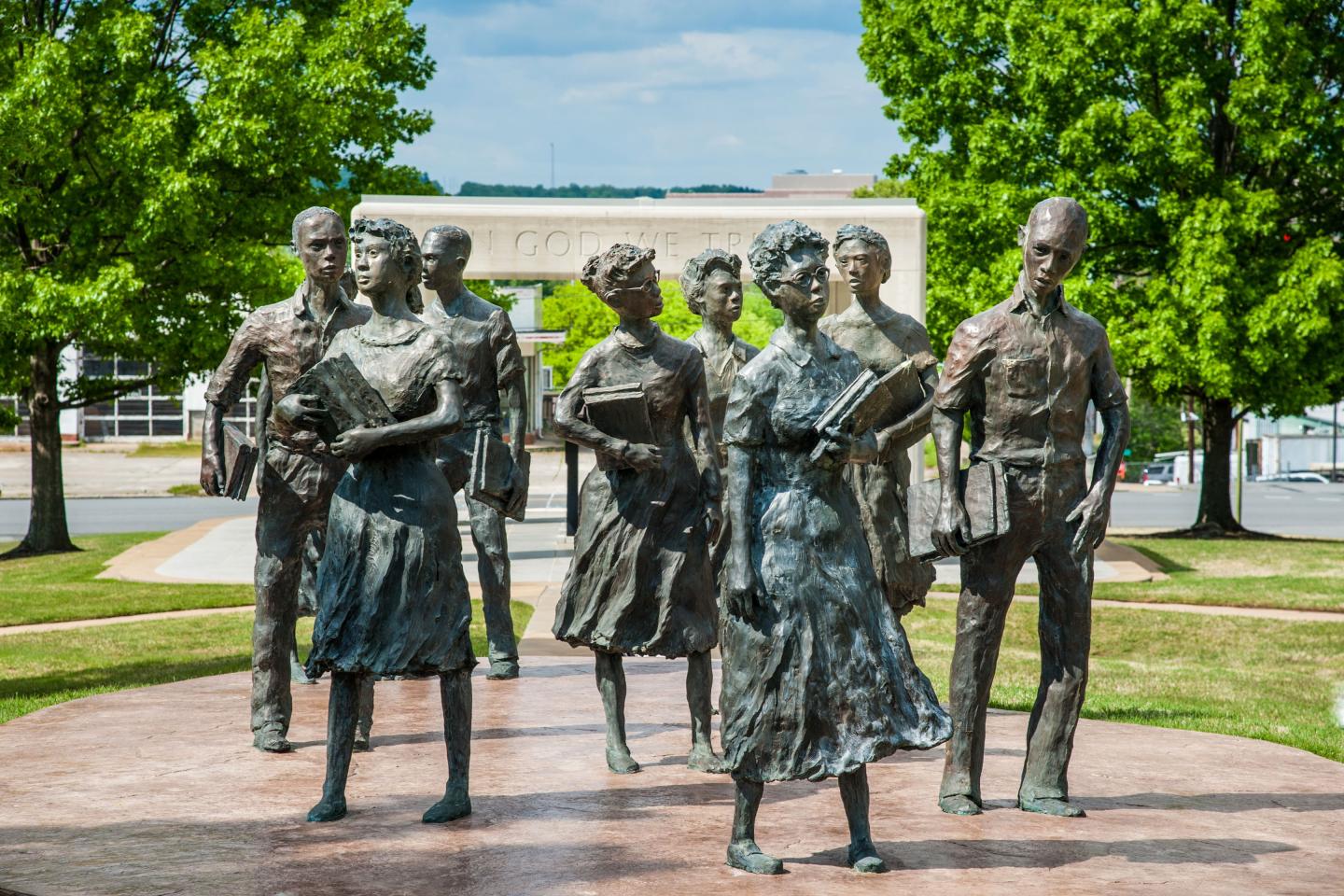 Bronze statues of nine students walking together, greenery in the background.