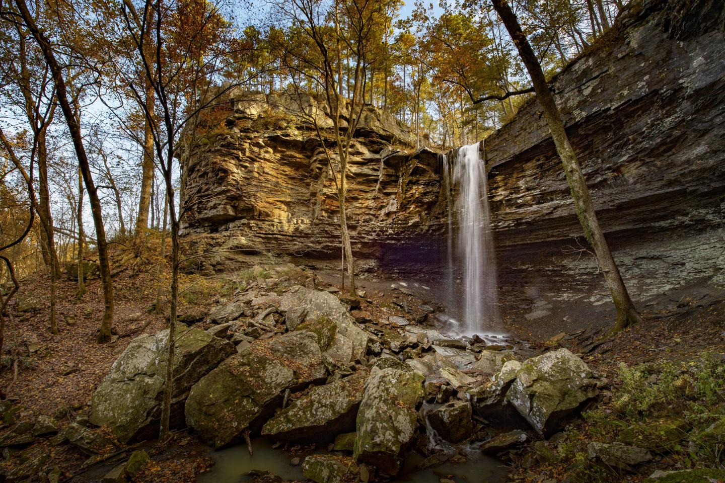 Waterfall cascading over rocky cliff amidst autumn trees.