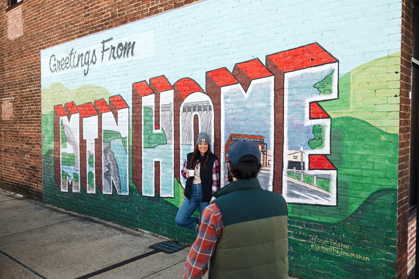 Colorful mural on brick wall with two people posing.