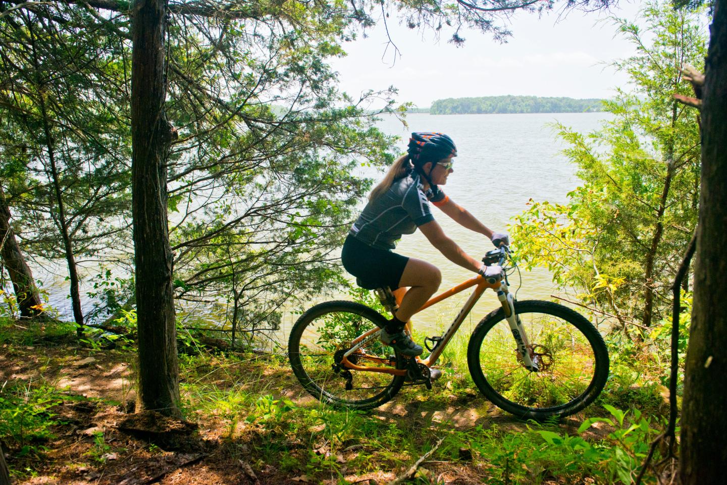 A person cycling on a forest trail near a lake on a sunny day.