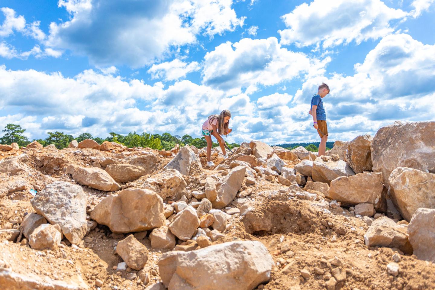 Children climbing rocks under a bright blue sky with clouds.