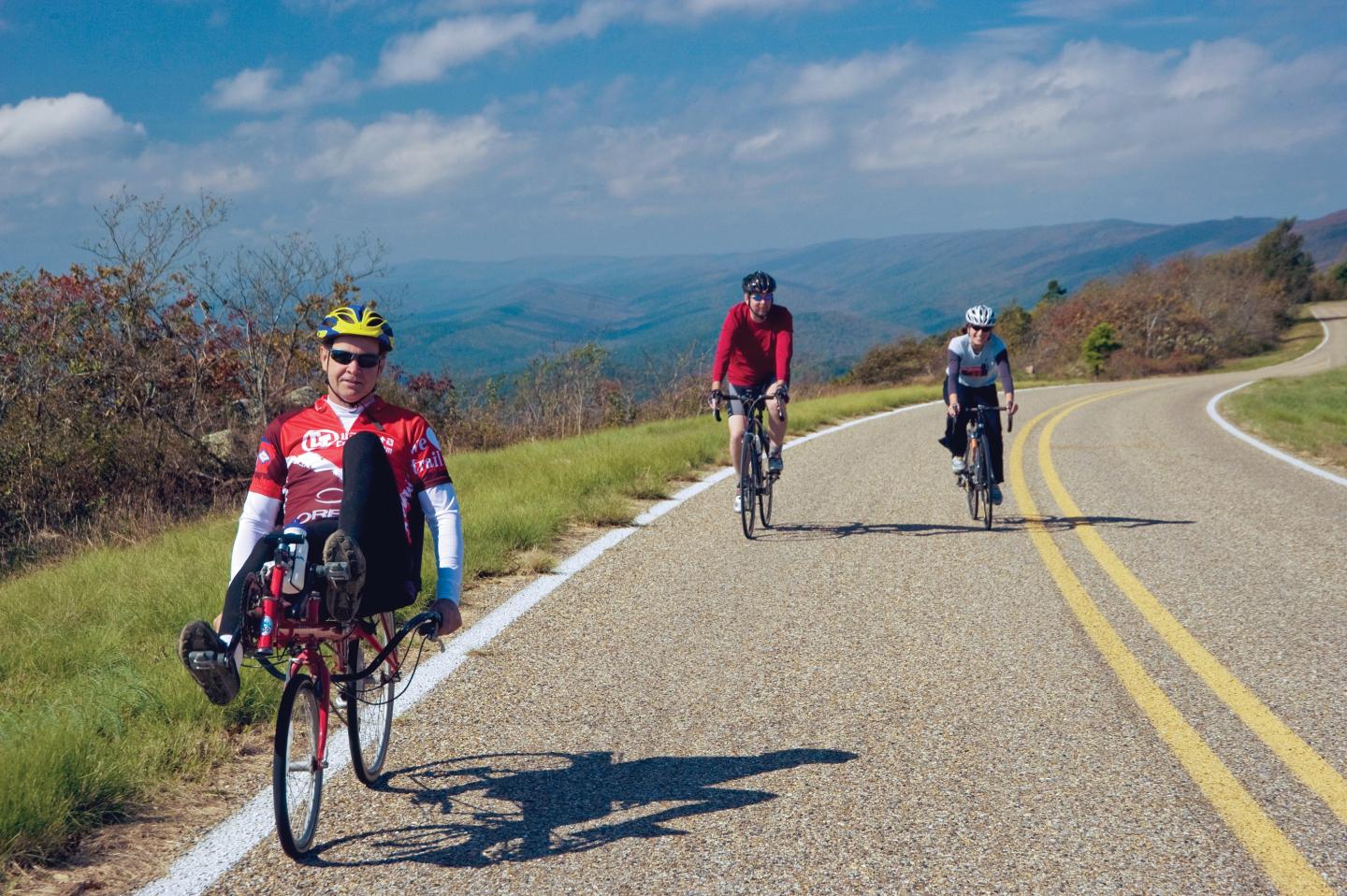 Cyclists riding on a scenic mountain road under a blue sky.