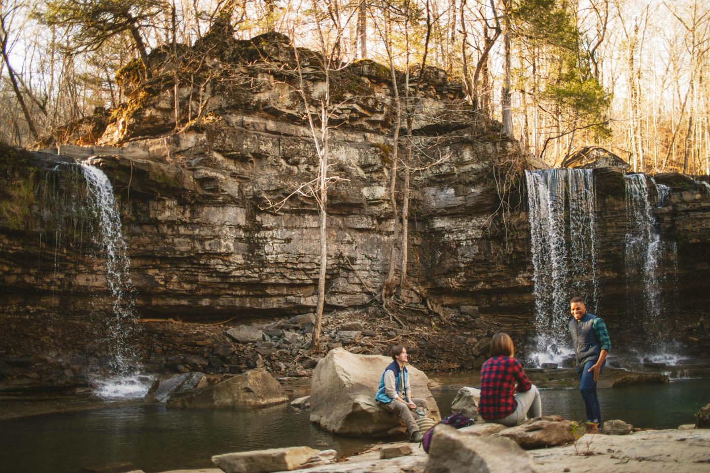 Three people sitting by waterfalls in a forest setting, enjoying nature.