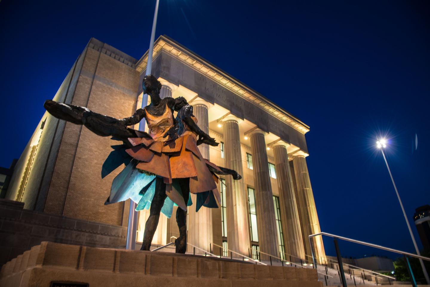 Two colorful abstract sculptures in front of a lit building at night.