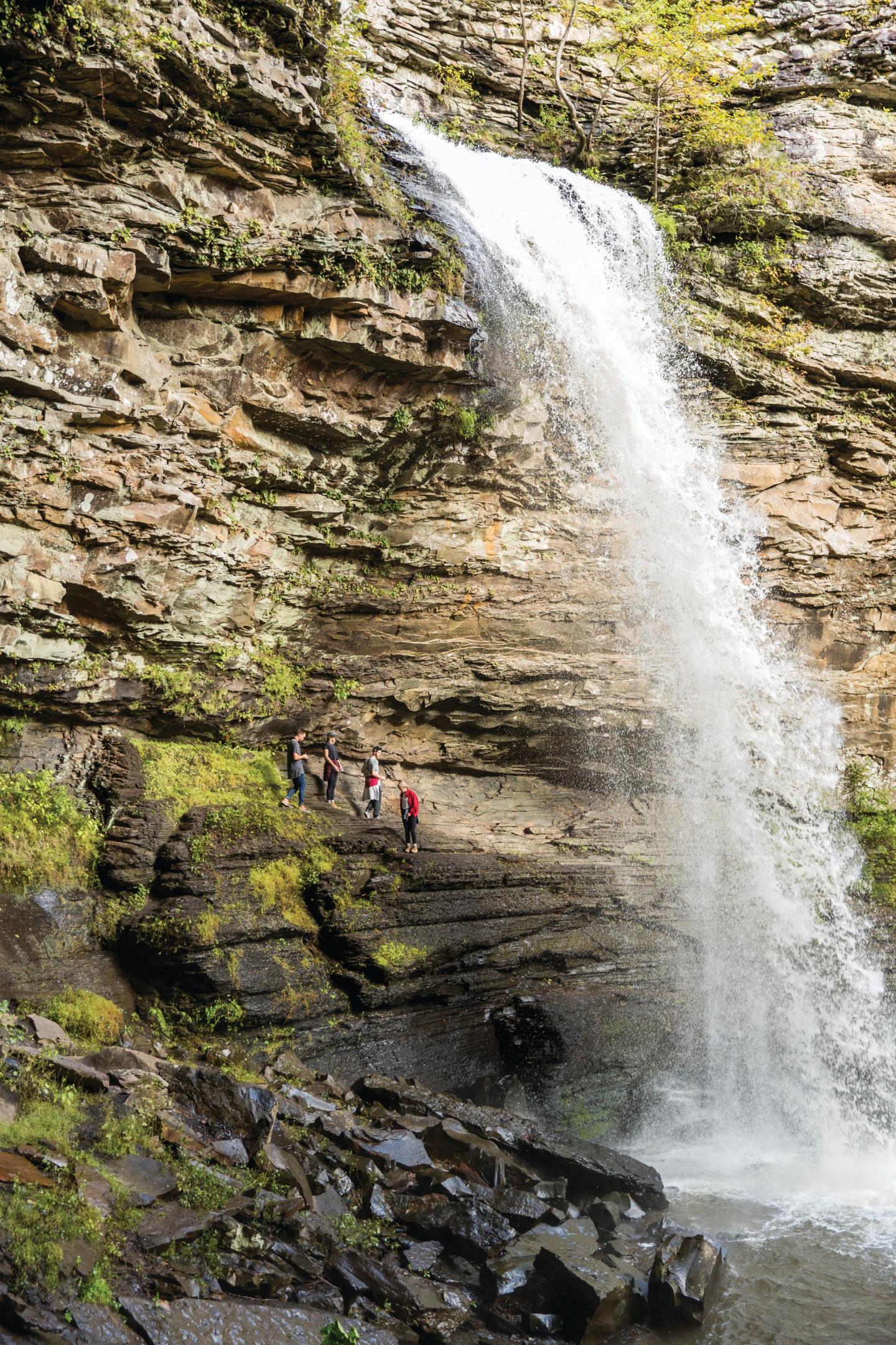 Waterfall cascading down rocky cliff, people standing nearby.