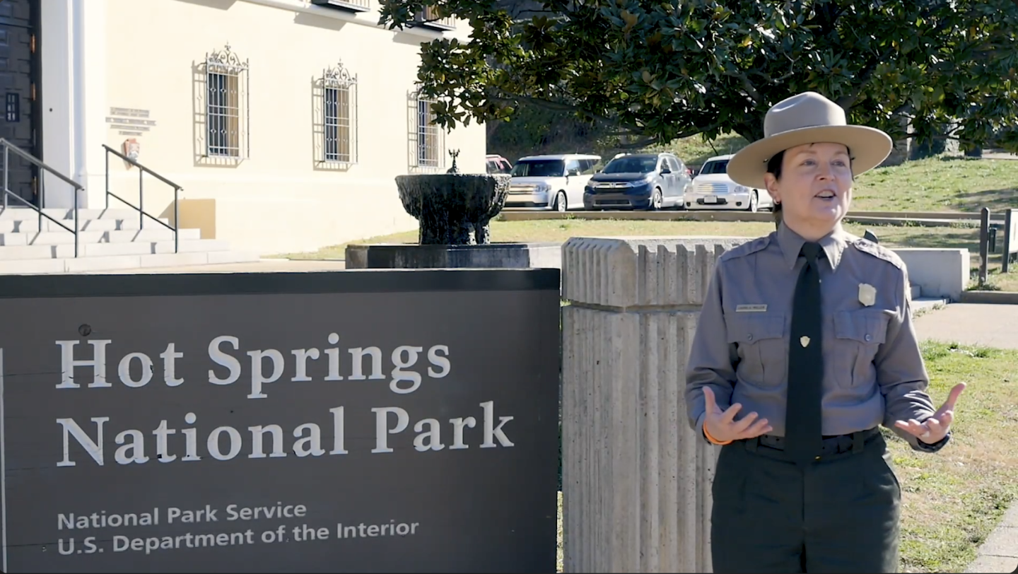 Park ranger stands beside the Hot Springs National Park sign.