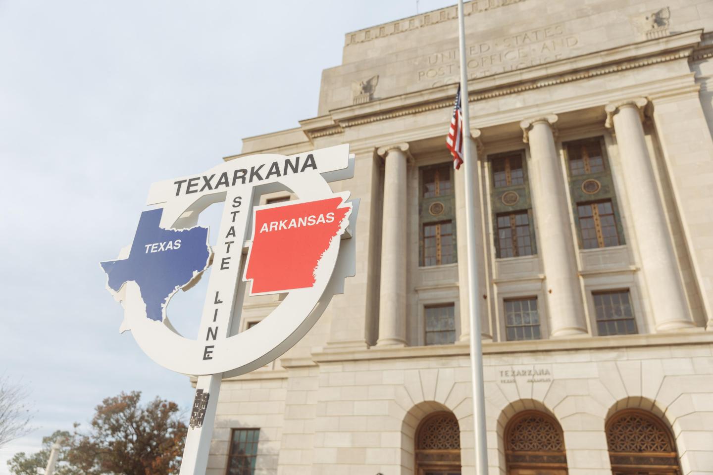 Texarkana sign showing Texas and Arkansas, near a historic building.