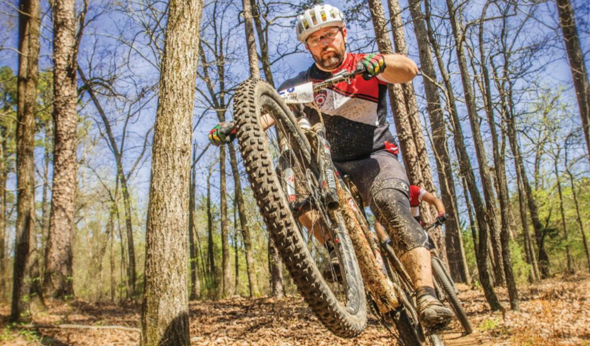 Mountain biker performs a wheelie on a forest trail.