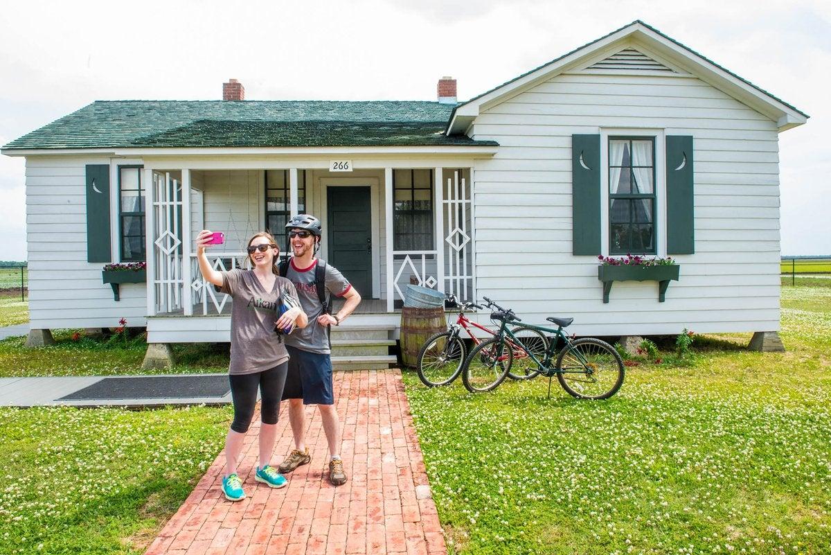 Couple posing with bicycles in front of a white house with green shutters.