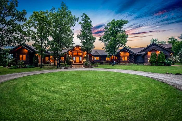 Luxury log cabin at dusk with glowing lights and green lawn.