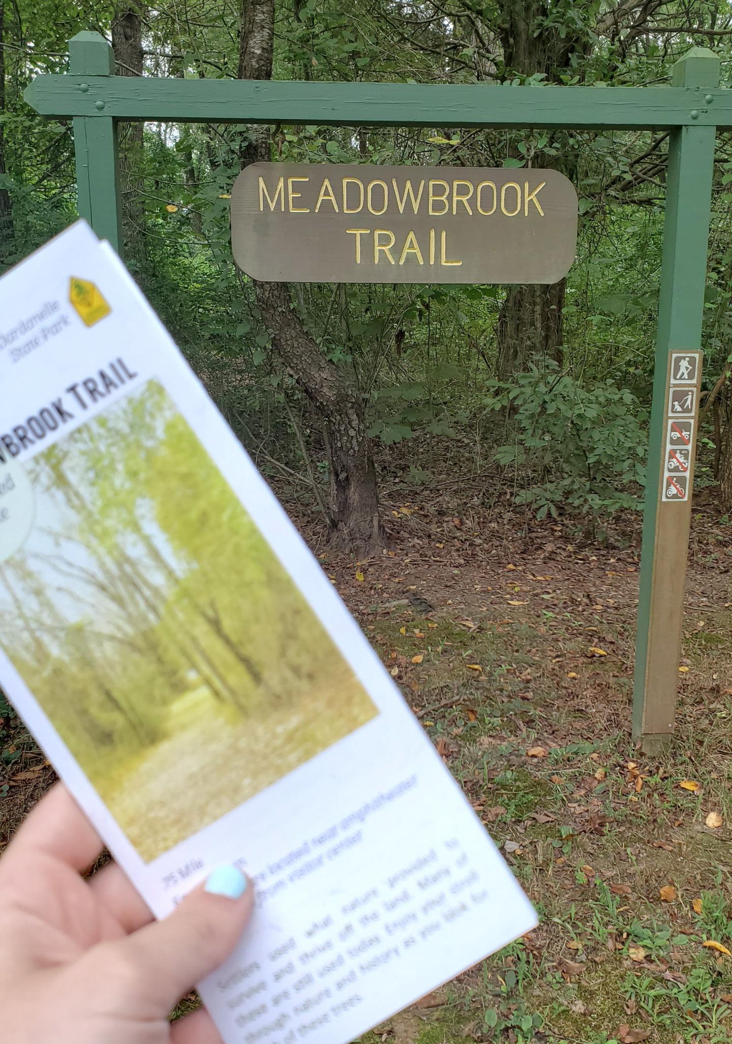 Trail entrance sign with a person holding a brochure in front.