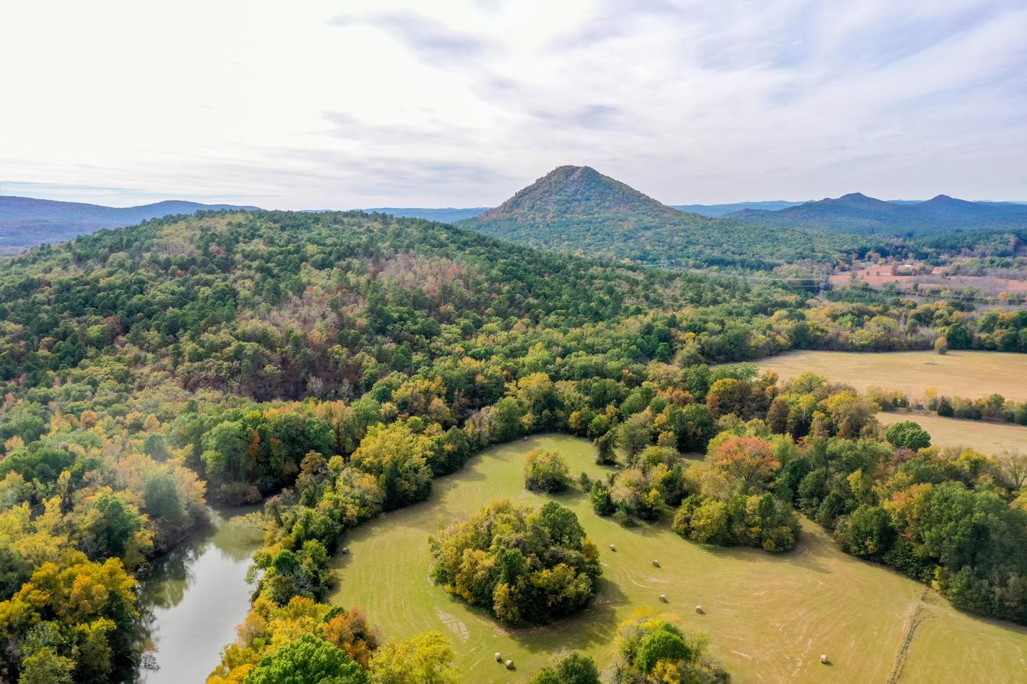 Aerial view of a green landscape with hills and a winding river under a cloudy sky.
