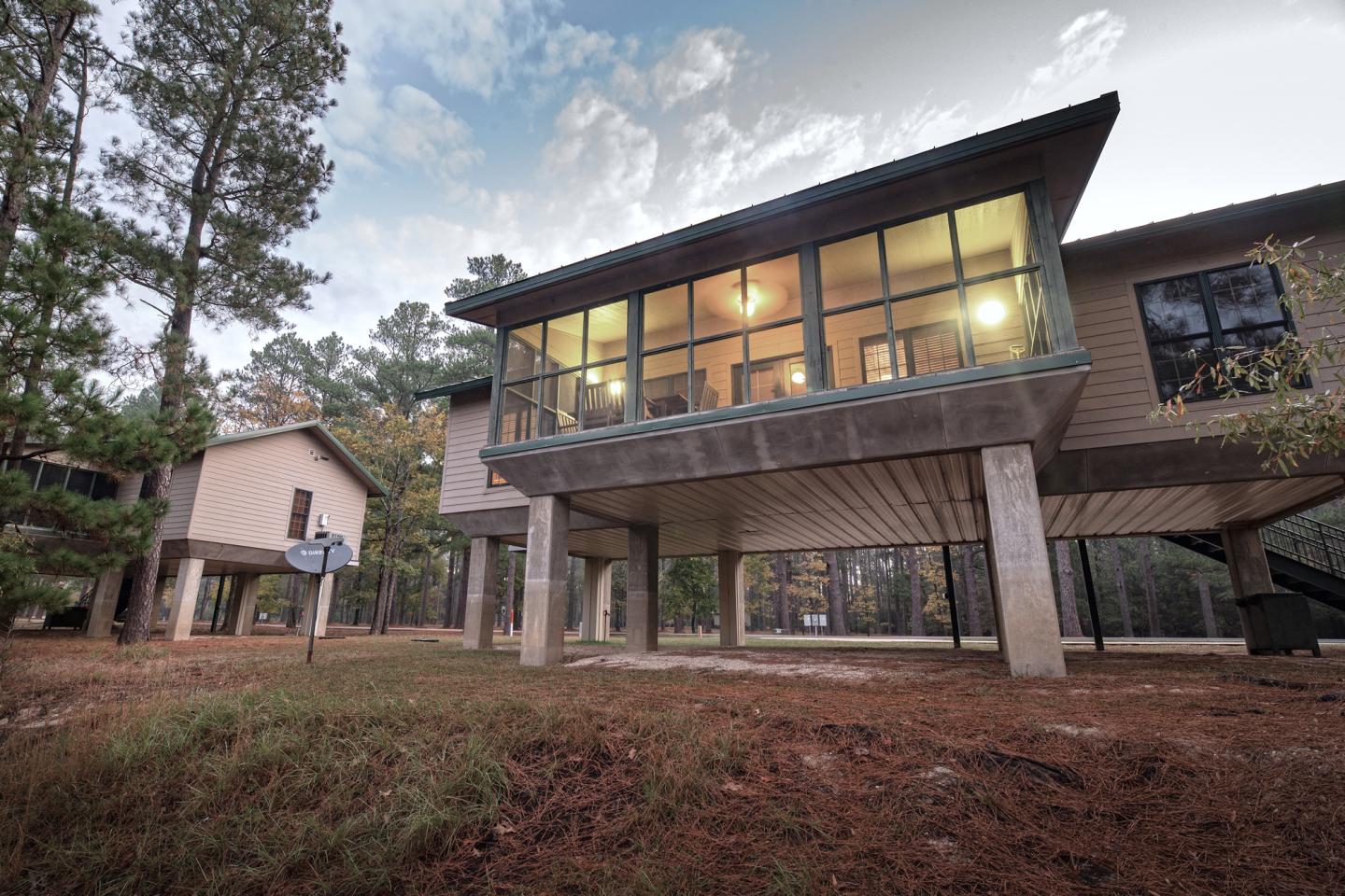 Modern raised cabin among tall trees, with large windows and evening lights.
