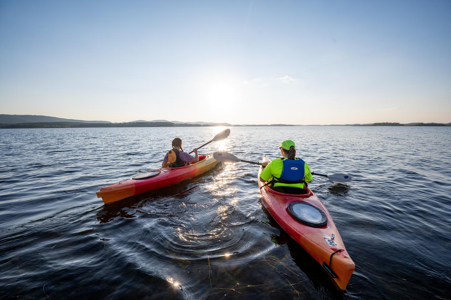 Two people kayaking on a lake at sunset.