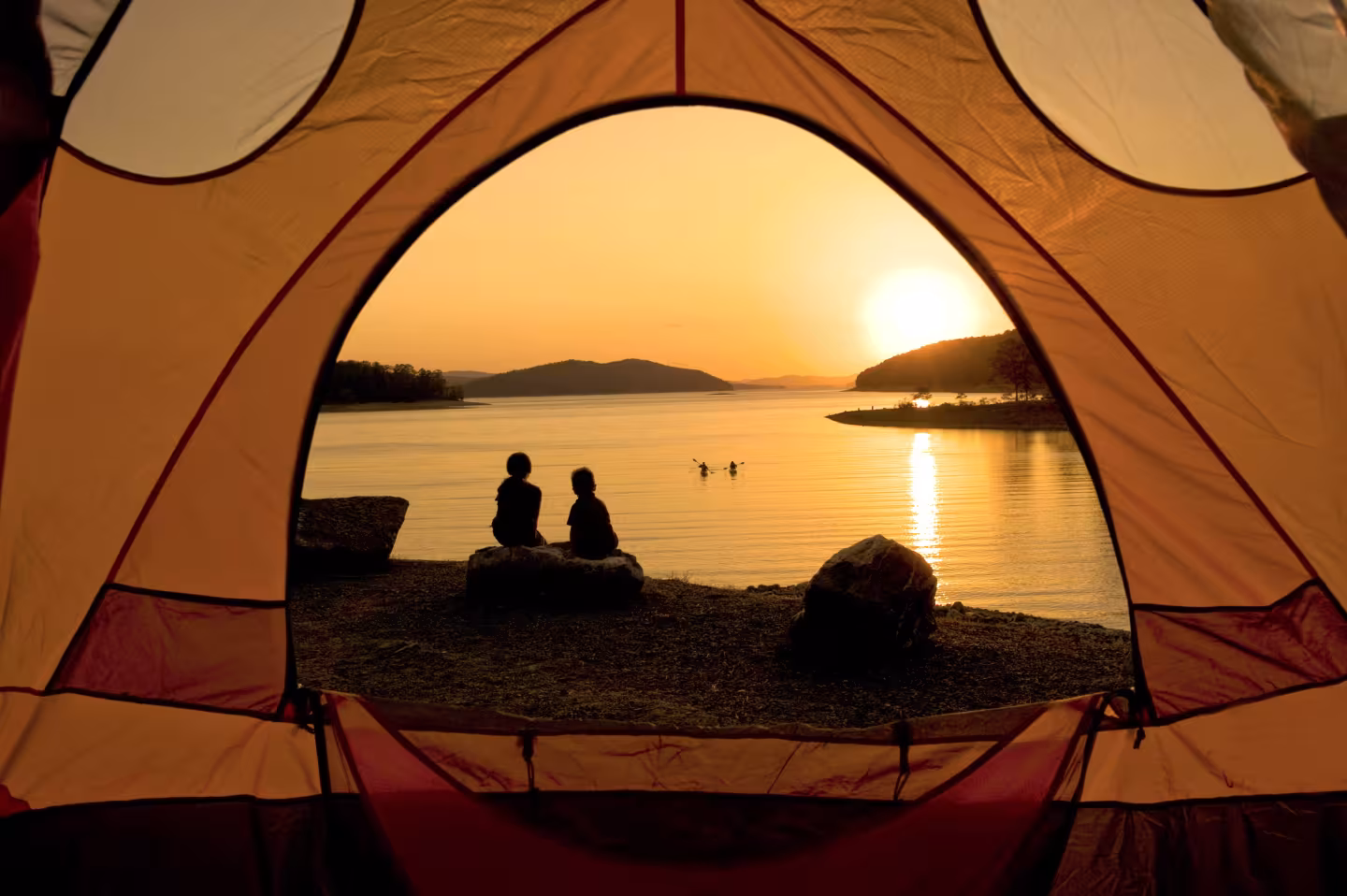 Sunset view from a tent, with two people by a lake.