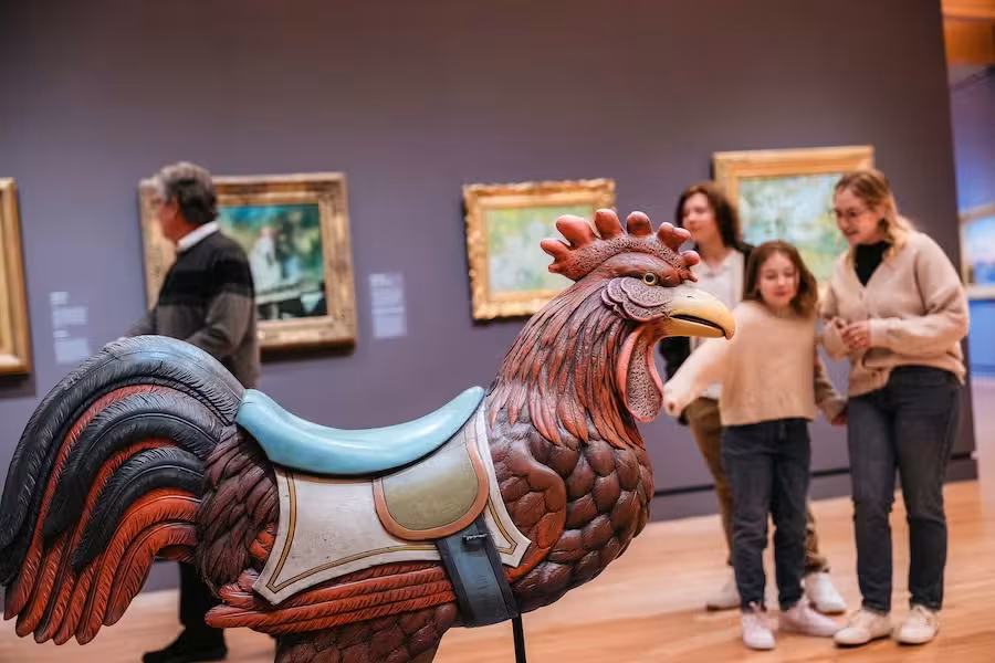 A family admires a large rooster sculpture in an art gallery.