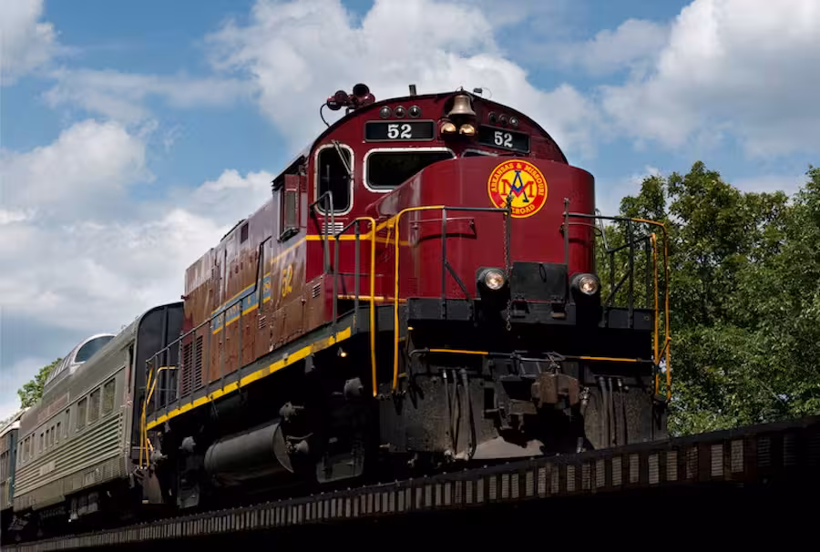 Red locomotive on a bridge under a cloudy sky.