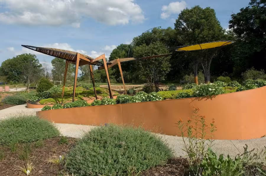 Modern garden with angular metal structures and lush greenery under a blue sky.