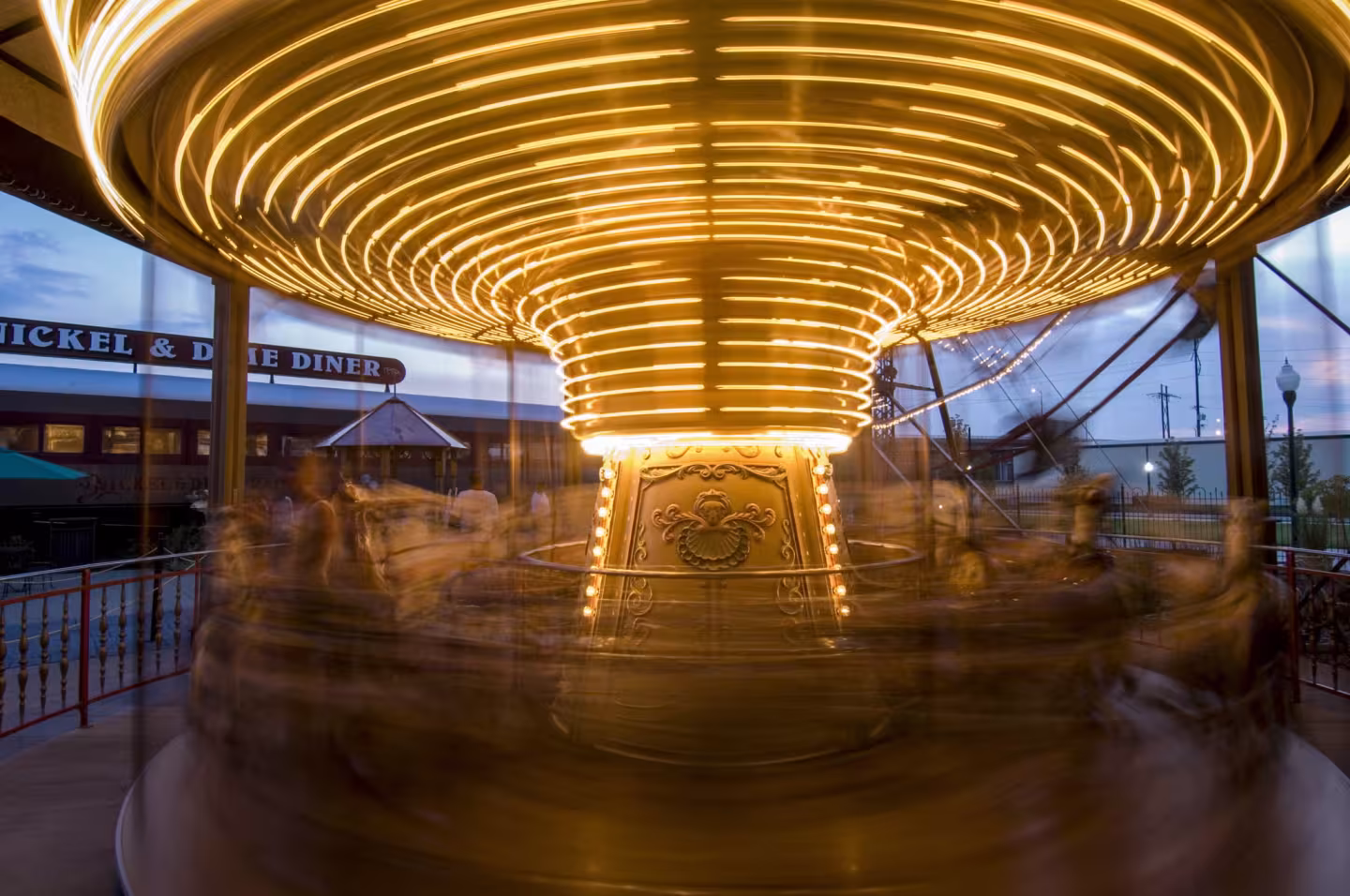 Carousel lit up at night, spinning with blurred figures, warm yellow lights illuminating.
