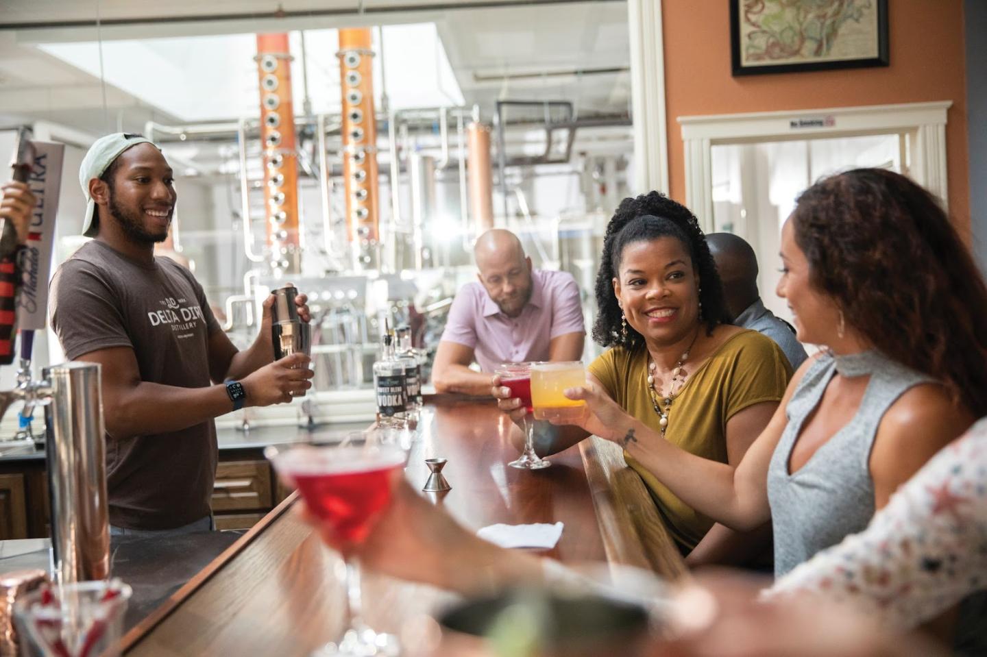 Bartender serving drinks to smiling patrons at a lively bar counter.