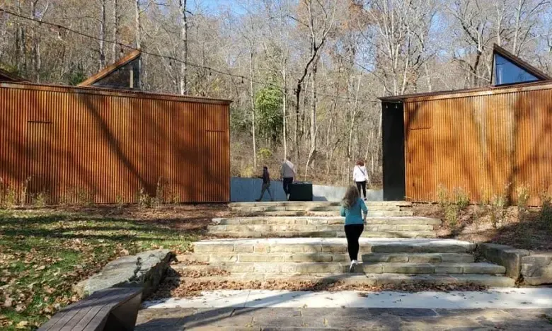 Wooden buildings surround steps with people walking in a wooded area.