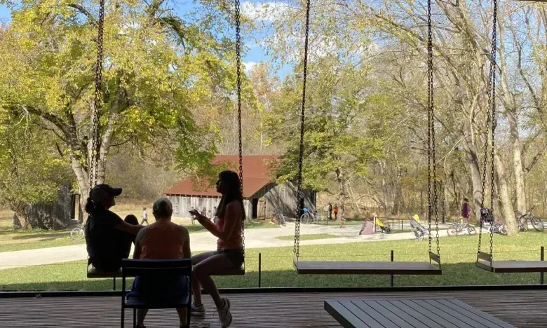 Three people, silhouetted, sitting indoors with a view of trees and a path outside.